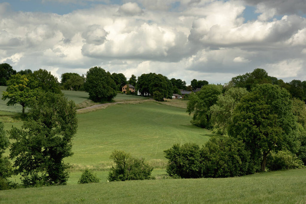 Rolling countryside with meadows, houses and trees under a cloudy sky. - Photo, image