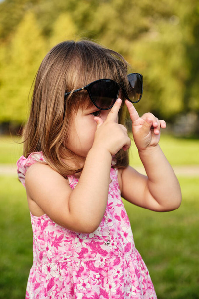 Little girl wearing mom's sunglasses. Portrait of a sweet baby girl who's stolen mom's sunglasses and happy to wear them trying to look like a grown up. - Foto, Imagem