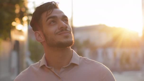 Close-up pensive inspired Indian Latin Arabic Hispanic bearded male boss worker man in formal shirt outdoors looking at sky thinking. Portrait businessman stands in city street in sunset sun dreaming - Filmagem, Vídeo