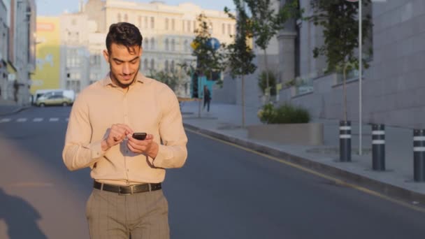 Happy smiling cheerful adult businessman boss manager entrepreneur employee man walking on street looking at screen phone chatting with smartphone going at road using mobile online map walks in city - Felvétel, videó