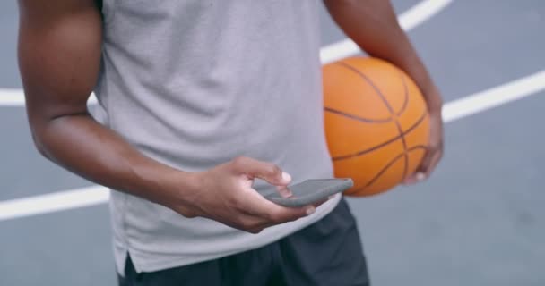 Phone, sport and basketball with a man on social media holding a ball on a sports court outside for training, exercise and workout. Fitness, health and 5g with a male athlete ready to play a game. - Video