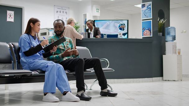 Diverse people doing consultation appointment in hospital reception, receiving healthcare support and advice to cure disease. Patient and asian nurse talking about recovery in waiting area. - Fotó, kép