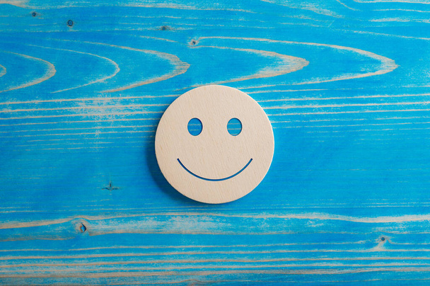 Улыбающееся выражение лица, вырезанное на деревянном круге, расположенном на голубом фоне. - Фото, изображение