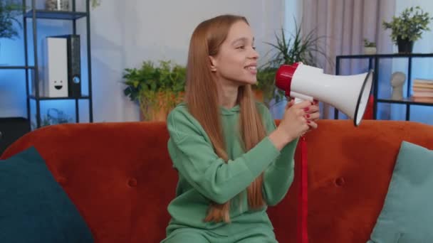 Portrait of teen girl talking with megaphone, proclaiming news, loudly announcing advertisement, warning using loudspeaker to shout speech. Young child kid at home apartment living room on couch - Filmagem, Vídeo