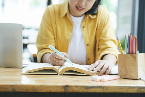 Ευτυχισμένη νεαρή Ασιάτισσα βαρετή να διαβάζει πολλά βιβλία. Φοιτητής σπουδάζει σκληρά εξετάσεις σε ένα σπίτι. - Φωτογραφία, εικόνα