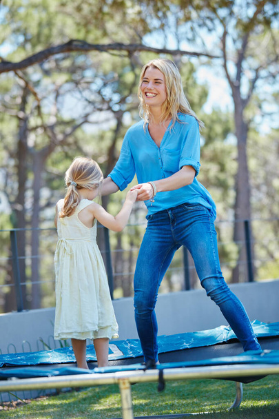 Jump around. a young mother playing on the trampoline with her daughter outside - Foto, afbeelding