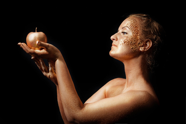 Девушка с золотым телом позирует с золотым яблоком в руках на черном
 - Фото, изображение