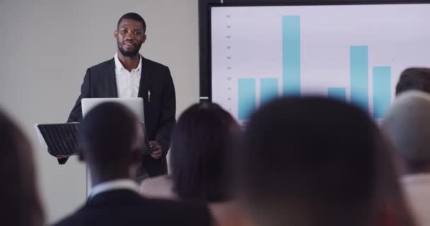 Business, conference and presentation of a black man at the office speaking to employee workers on a podium. Successful African corporate male presenting graph or chart for company goals in workshop - Materiaali, video
