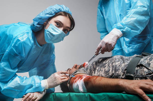 Shot of surgeon specialist and his assistant bandaging wounded military man. - Photo, Image