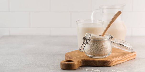  A jar of raw rice and rice milk in a glass on a plank on a gray background. Healthy food concept, alternative milk. Copy space - Φωτογραφία, εικόνα