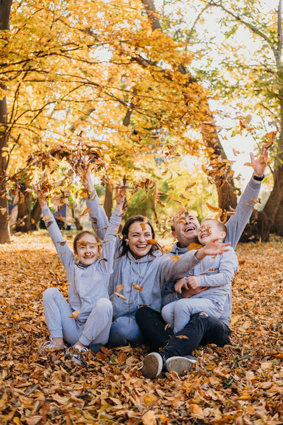 Portrait of a family taking group photos while happily throwing dry leaves of different colours in the air, spending time together during autumn. Family - Fotografie, Obrázek