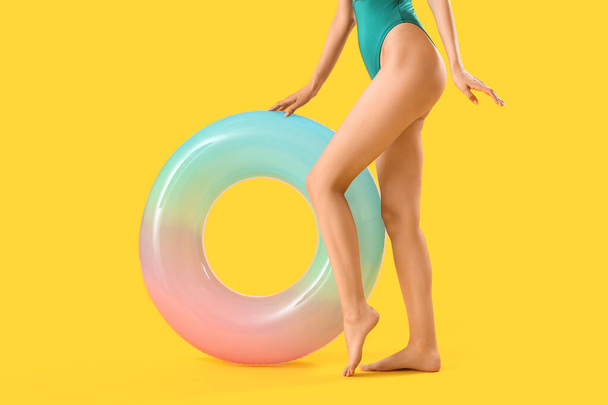 Beautiful young woman in swimsuit and with inflatable ring on yellow background - Zdjęcie, obraz