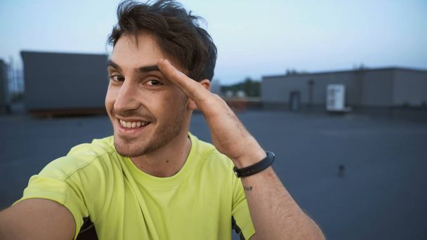 Smiling sportsman looking at camera and gesturing on roof in evening  - Foto, imagen