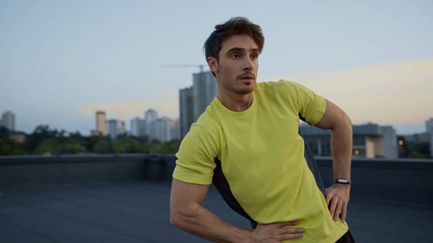 Young sportsman in yellow sportswear training on roof of building in evening  - Zdjęcie, obraz