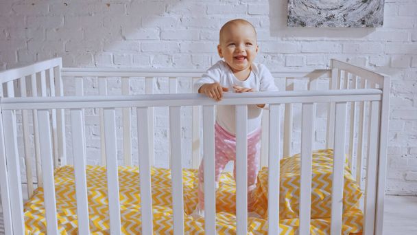 happy infant child standing in baby crib and smiling near brick wall - 写真・画像