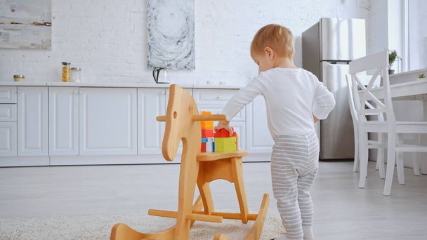 toddler kid playing with building blocks on rocking horse in spacious apartment - Fotoğraf, Görsel
