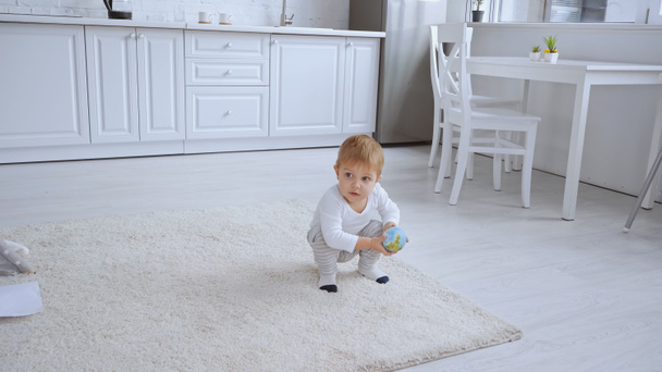 toddler boy sitting on carpet and holding small globe in spacious room - Foto, imagen