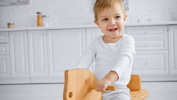 happy toddler boy laughing and riding wooden rocking horse at home   - Foto, afbeelding