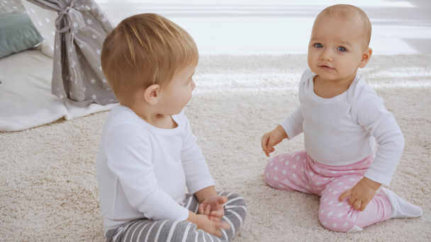 toddler brother looking at sister while sitting together on carpet at home - Foto, Imagen