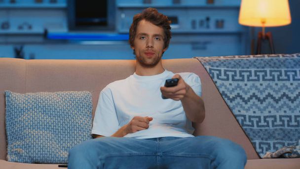 young man using remote controller while watching tv on couch - Photo, Image