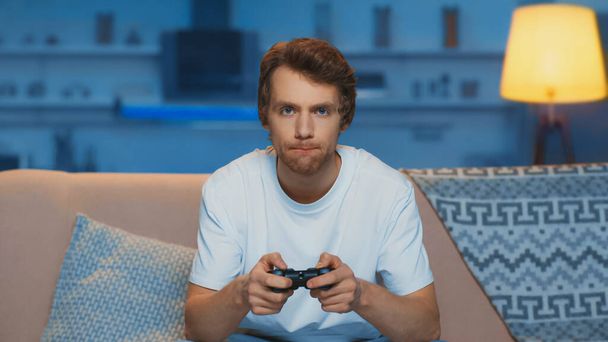 KYIV, UKRAINE - MARCH 12, 2019: focused young man playing video game in living room - Foto, immagini