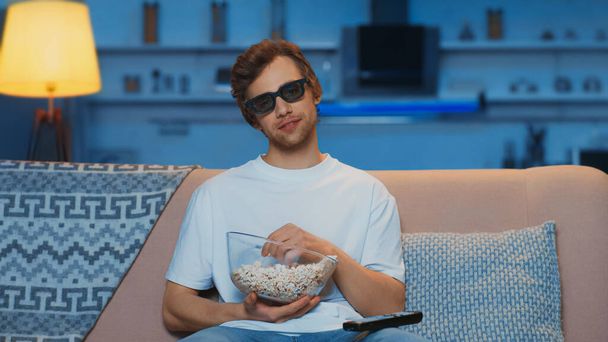 задоволений чоловік у 3d окулярах тримає чашу з попкорном під час перегляду фільму у вітальні
 - Фото, зображення