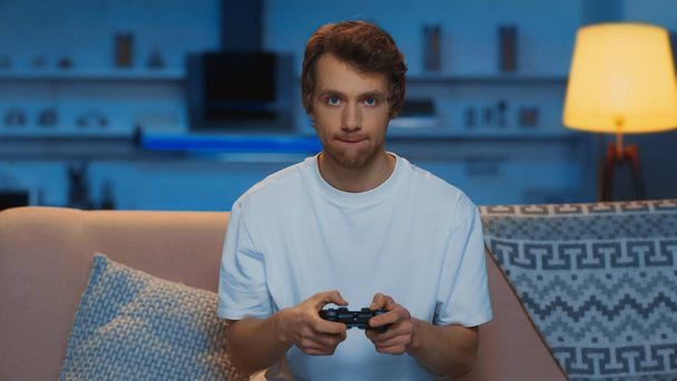 KYIV, UKRAINE - MARCH 12, 2019: concentrated young man playing video game in living room  - Photo, Image