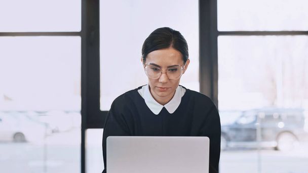focused businesswoman in eyeglasses working on laptop in office - Foto, afbeelding