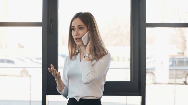 shocked woman talking on mobile phone and gesturing in office - Foto, afbeelding