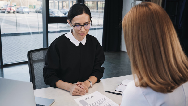 woman holding resume near businesswoman in eyeglasses during job interview - Photo, Image