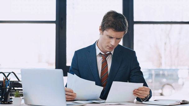 thoughtful businessman working with documents near laptop in office - Foto, imagen