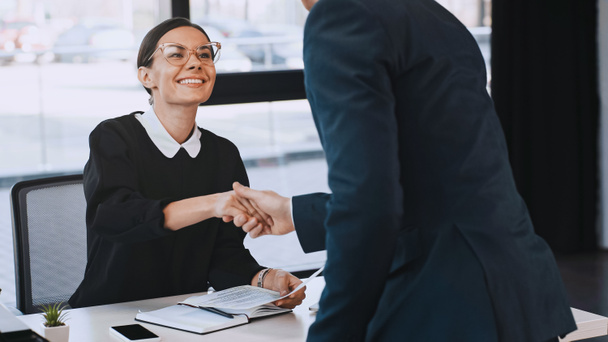 smiling businesswoman holding resume and shaking hands with man after job interview - Photo, Image