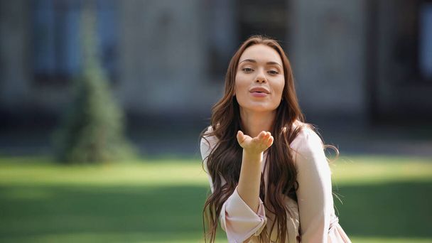 Young brunette woman blowing air kiss at camera in park  - Photo, Image