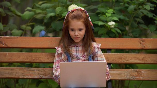 Amazed redhead kid using laptop on bench in park  - Foto, afbeelding