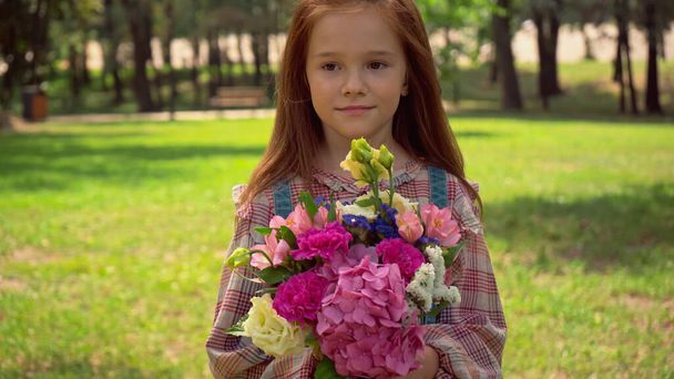 Redhead preteen child holding bouquet in park  - Valokuva, kuva
