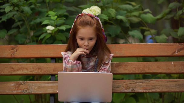 Shocked preteen child looking at laptop on bench in park  - Valokuva, kuva