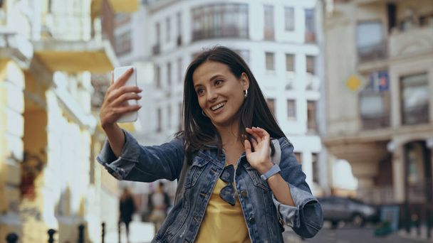 Smiling woman having video call on smartphone on urban street - Фото, изображение
