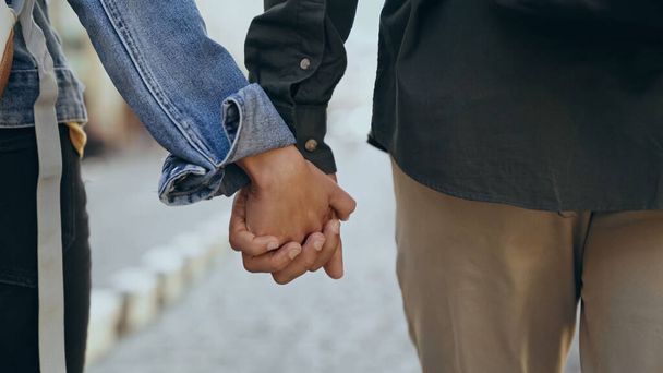 Cropped view of multiethnic couple holding hands on urban street  - Foto, Bild