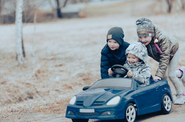 Üç mutlu çocuk kırsalda, dışarıda büyük oyuncak arabalarla oynuyorlar.. - Fotoğraf, Görsel