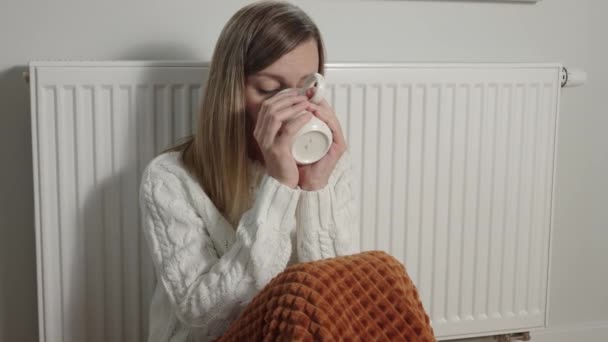 Worried sad woman sits under blanket near heating radiator with cup of tea, Rising costs in private households for gas bill due to inflation and war, Energy crisis in Europe - Materiaali, video