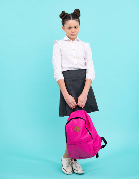 Unhappy sad teenager school girl. Schoolgirl in school uniform with school bag. Teenage girl student on blue isolated background. Learning knowledge and children education concept - Photo, image