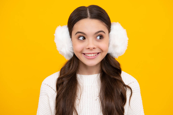 Teenager girl with winter warm earmuff ear-flaps over isolated yellow background. Winter christmas holidays, new year mood. Kids warm clothes. Happy face, positive and smiling emotions of teenager - Foto, imagen