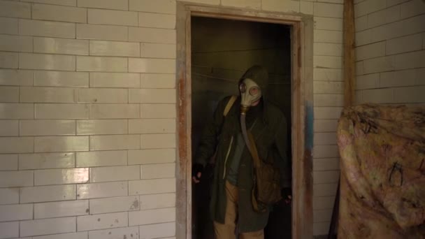 Een stalker in militaire kleding en een gasmasker die door een verlaten gebouw loopt. begrip overleving na de apocalyps - Video
