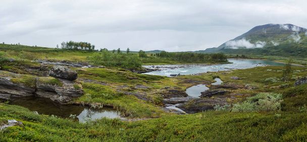 Panoramic view of blue glacial Arasjahka river rapids in Lapland landscape with green mountains and birch trees at Padjelantaleden hiking trail, north Sweden wild nature. Summer cloudy day. - Foto, Bild