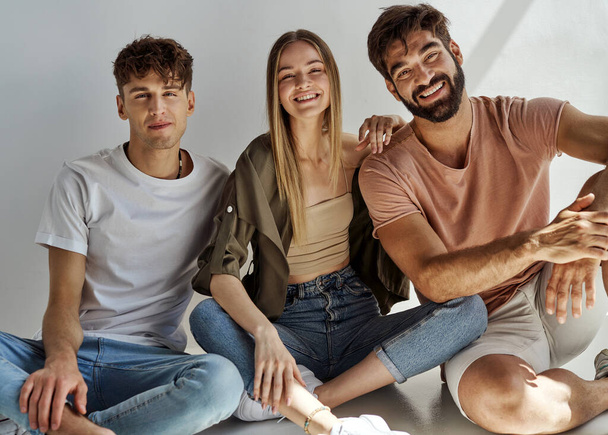 Group of three friends in daily outfit sitting and smiling to the camera - Photo, image
