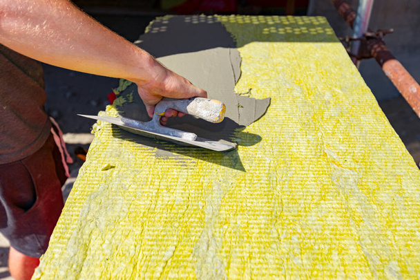 View on worker's hand with trowel, applying glue on yellow mineral wool for insulation the building under construction.  - Fotó, kép