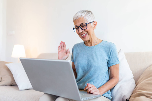 Прогресивний пенсіонер. Розумна захоплена прогресивна старша жінка розмахує рукою і відчуває себе щасливою, використовуючи відеодзвінок у своєму ноутбуці і розмовляючи з онуками
 - Фото, зображення