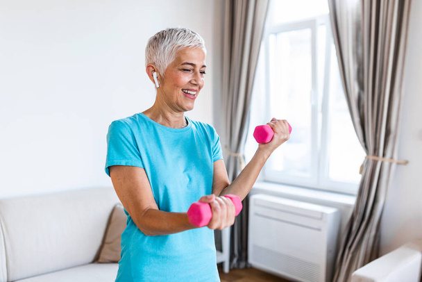 Senior woman exercise with dumbbells at home . happy mature woman doing arm workout using dumbbells. Elderly woman prefers healthy lifestyle - Fotó, kép