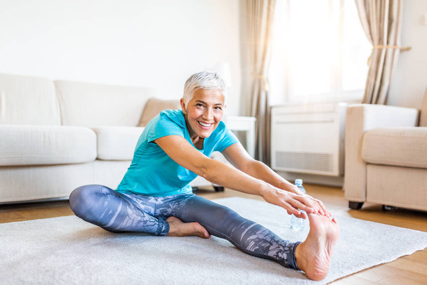senior woman doing warmup workout at home. Fitness woman doing stretch exercise stretching her legs,quadriceps .Elderly woman living an active lifestyle. - Fotoğraf, Görsel