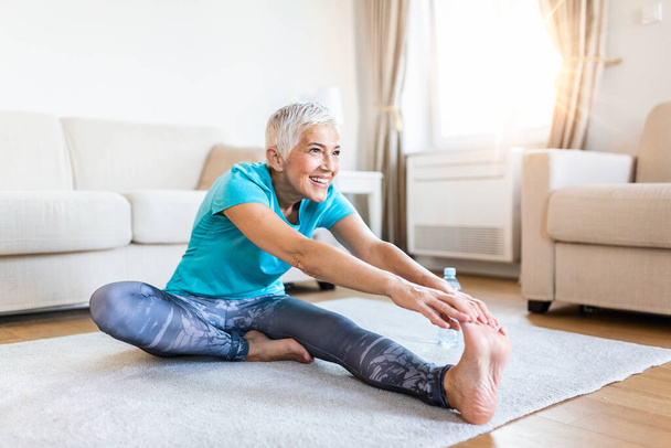 senior woman doing warmup workout at home. Fitness woman doing stretch exercise stretching her legs,quadriceps .Elderly woman living an active lifestyle. - Valokuva, kuva